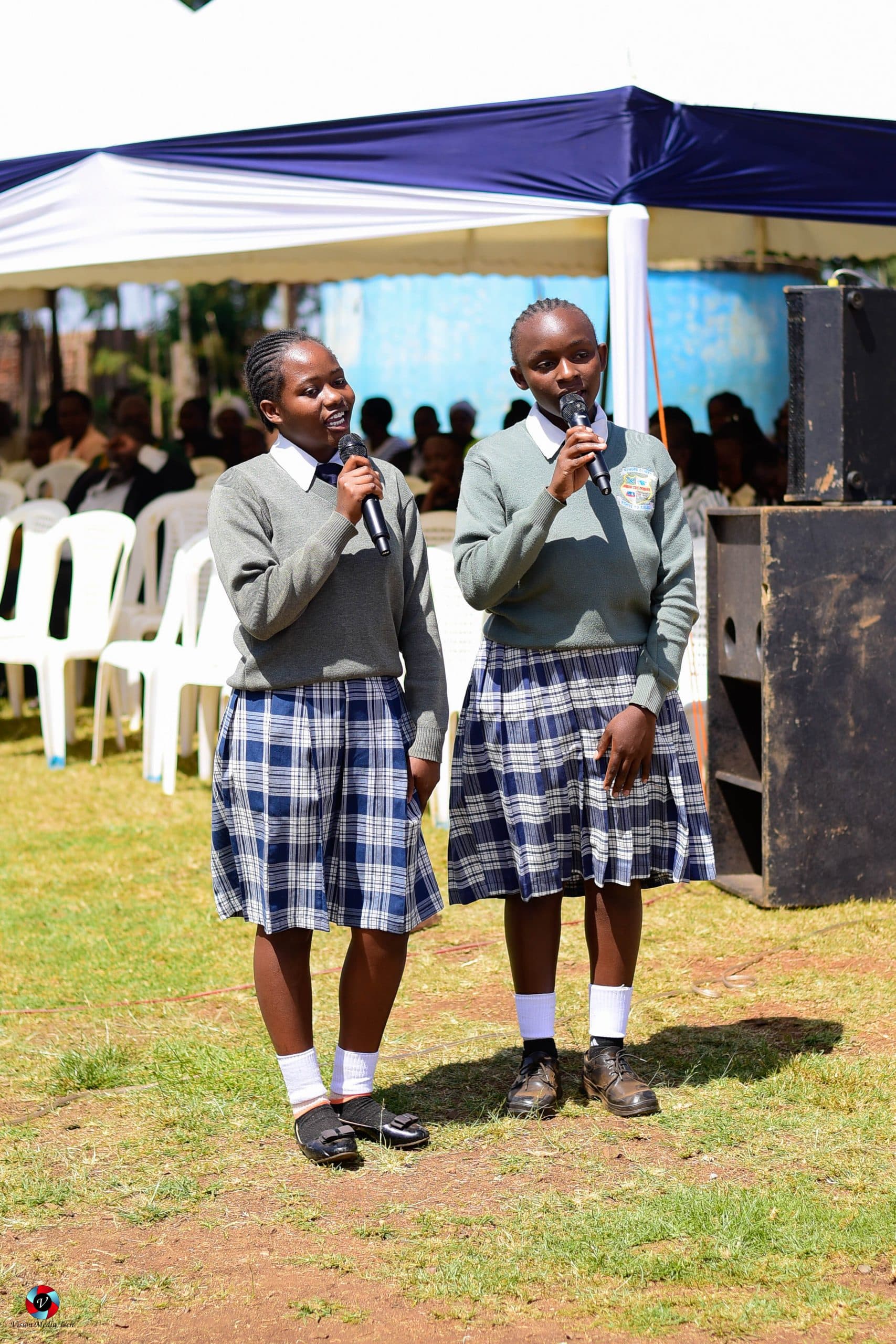 Two students speaking into microphones at a school gathering
